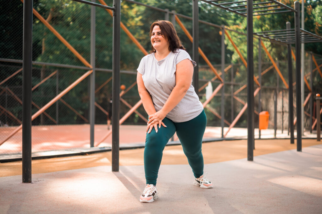 smiling woman with overweight tracksuit doing exercises sports field park